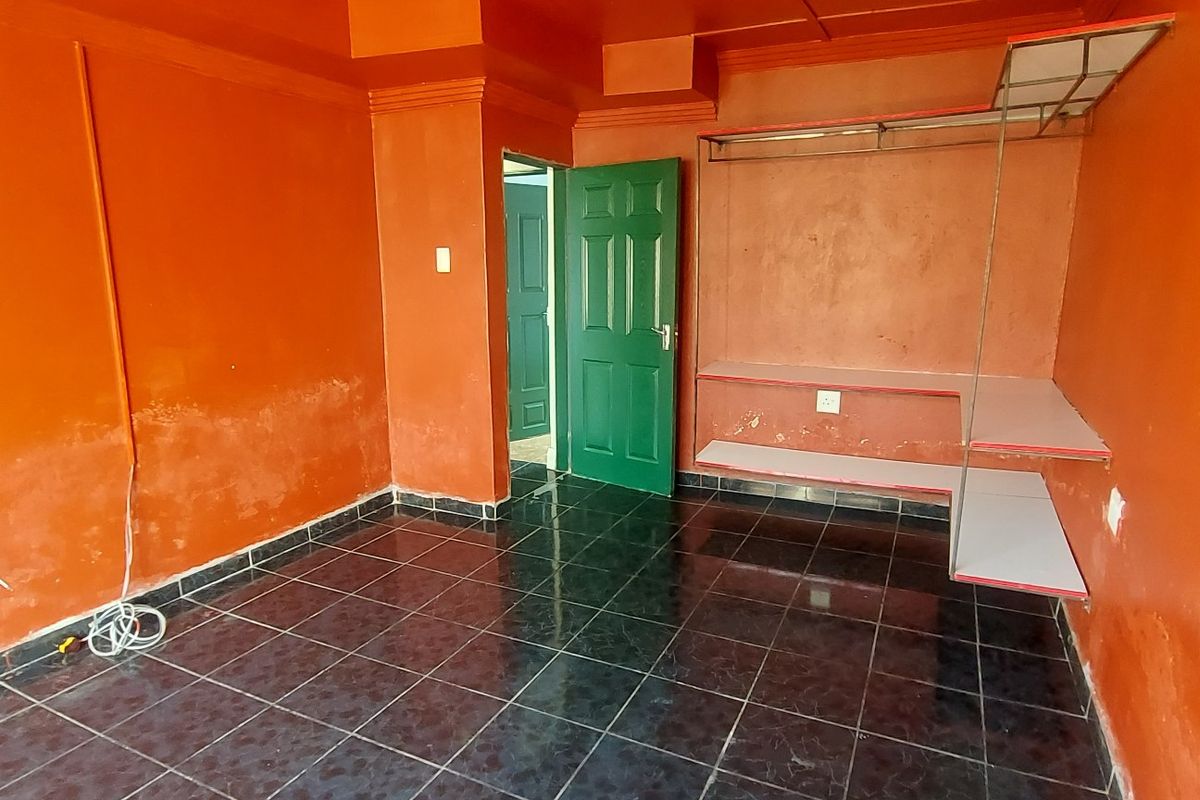 An empty bedroom featuring dark tiled flooring, built-in shelving, and vibrant orange walls requiring maintenance and cosmetic updates.