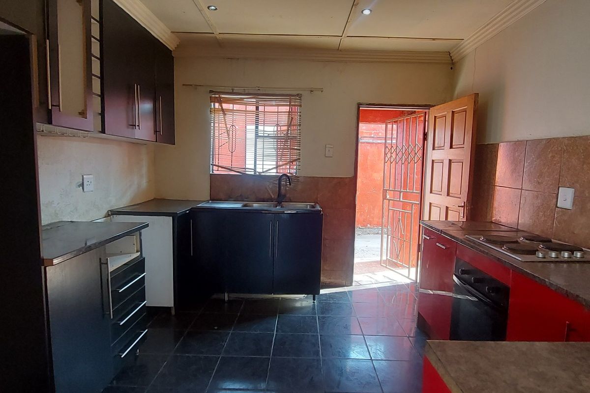 A functional kitchen featuring built-in cabinetry, a built-in oven with hob, tiled flooring, and direct access to an exterior area via a security gate.