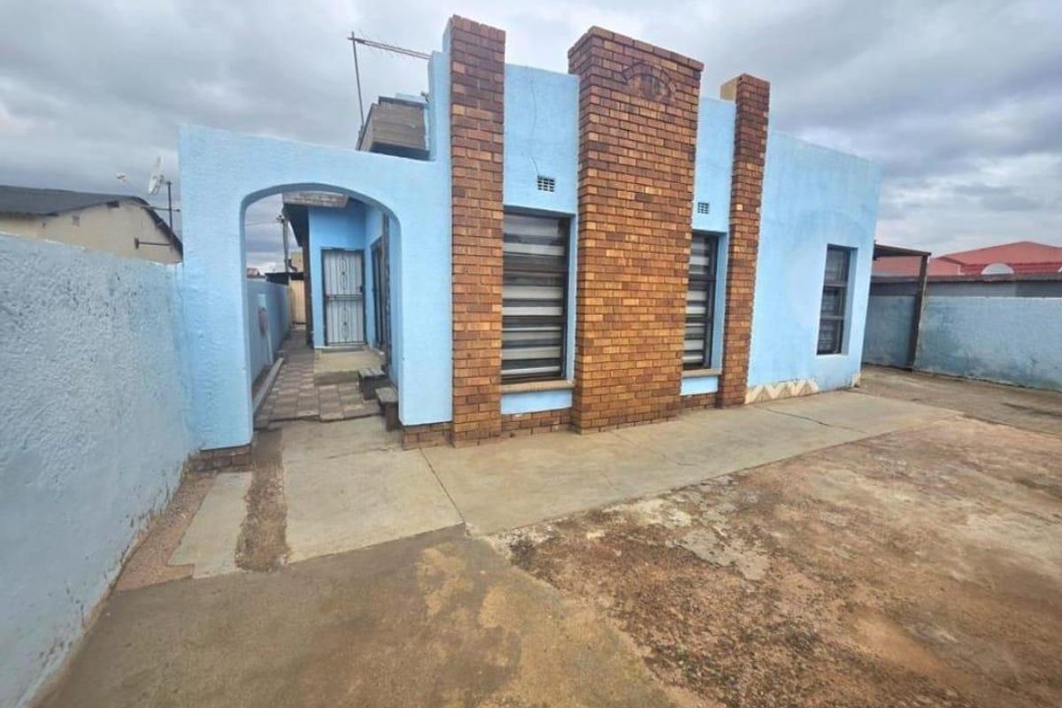 Rear exterior view of the house featuring a combination of brick and blue plastered walls with concrete paving.