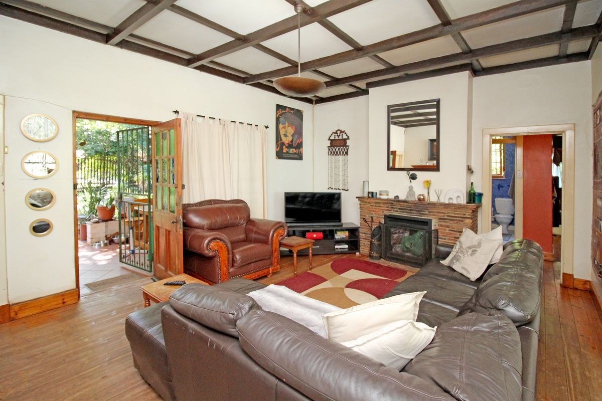 Living room featuring exposed timber ceiling beams, a brick fireplace, and hardwood flooring, with direct access to an outdoor patio area.