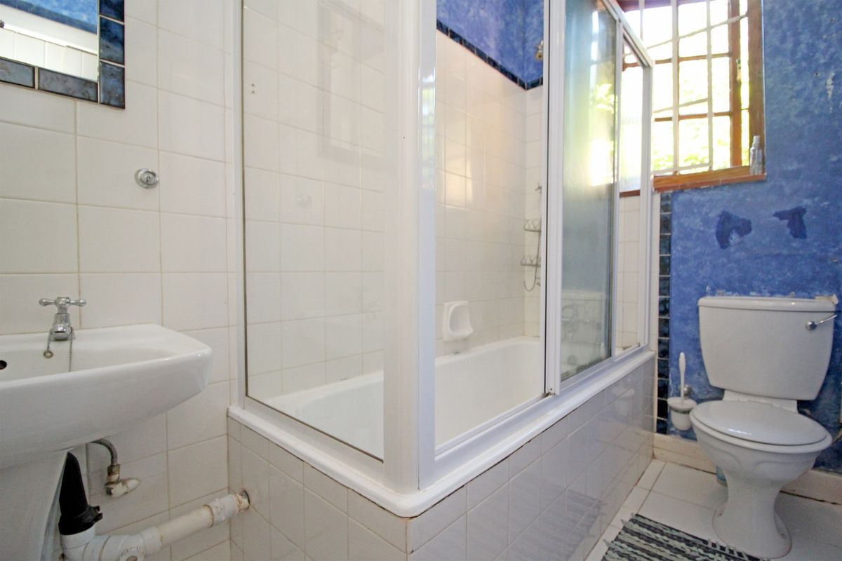 A dated bathroom featuring a shower-over-bath combination, pedestal basin, and toilet, with blue accent walls and white tiling throughout.