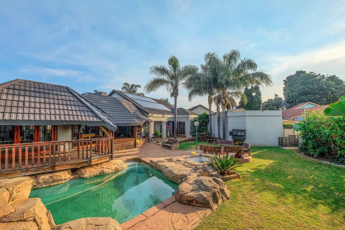 Rear garden featuring a rock-edged swimming pool, wooden deck, built-in braai area, and solar panels on the tiled roof.