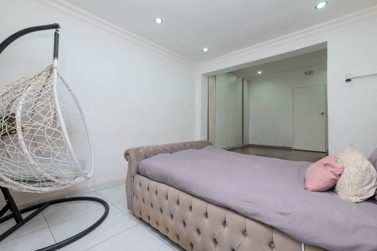 A spacious bedroom featuring tiled flooring, recessed downlighting, coved cornicing, and integrated built-in cupboards for storage.