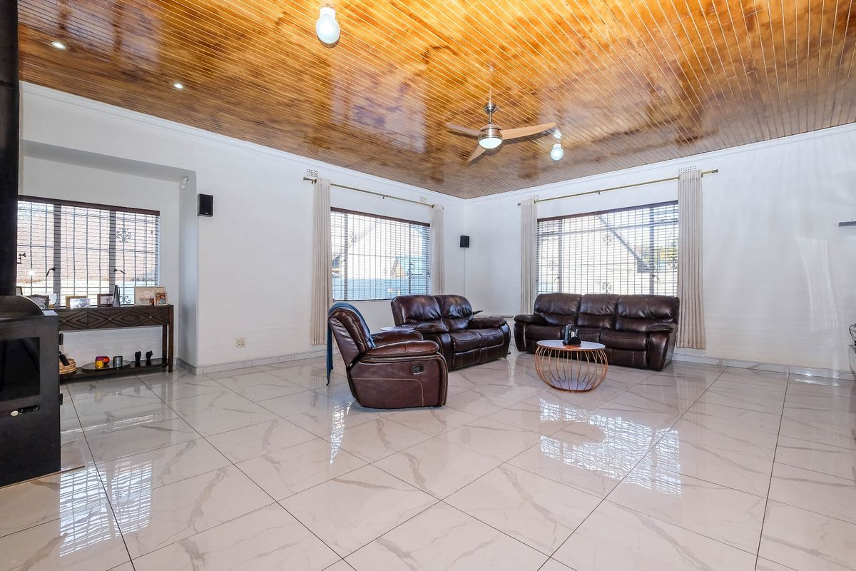 Spacious living room featuring polished porcelain floor tiles, a distinctive timber tongue and groove ceiling, ceiling fan, and a built-in wood burning fireplace.