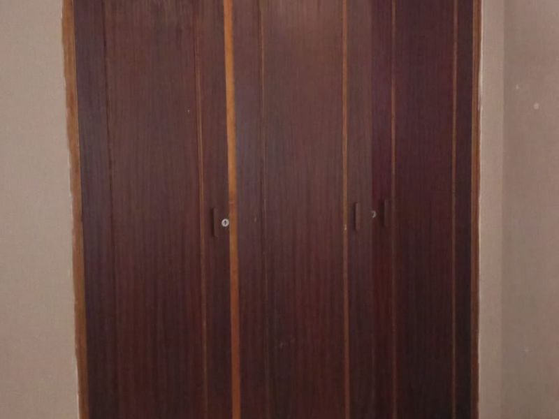 A bedroom featuring a large built-in wooden wardrobe and tiled flooring, offering a functional storage solution in need of cosmetic updates.