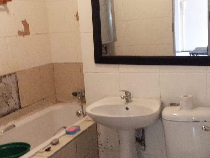 A dated bathroom featuring a pedestal basin, toilet, and bathtub with visible wall damage and worn tiling requiring renovation.
