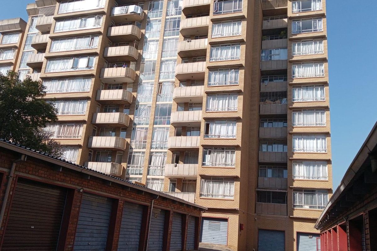 Exterior view of a multi-story apartment building featuring brick facade, multiple balconies, and ground-level garage units.