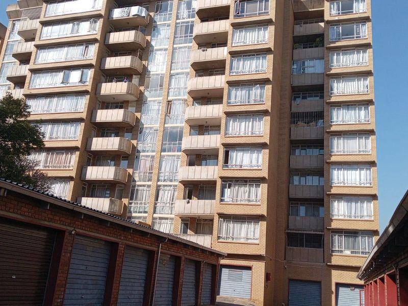 Exterior view of a multi-story apartment building featuring brick facade, multiple balconies, and ground-level garage units.