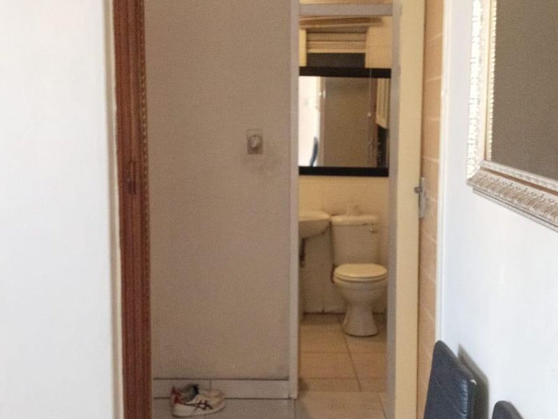 A narrow hallway featuring tiled flooring and a built-in cupboard, providing access to an adjacent bathroom area.