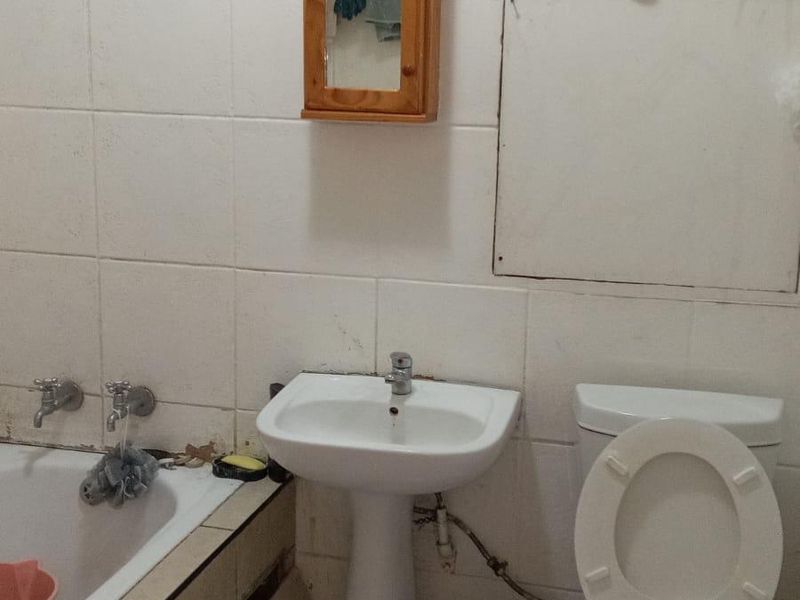 A functional bathroom featuring a pedestal basin, toilet, and bathtub with tiled finishes, requiring some maintenance and cosmetic updates.