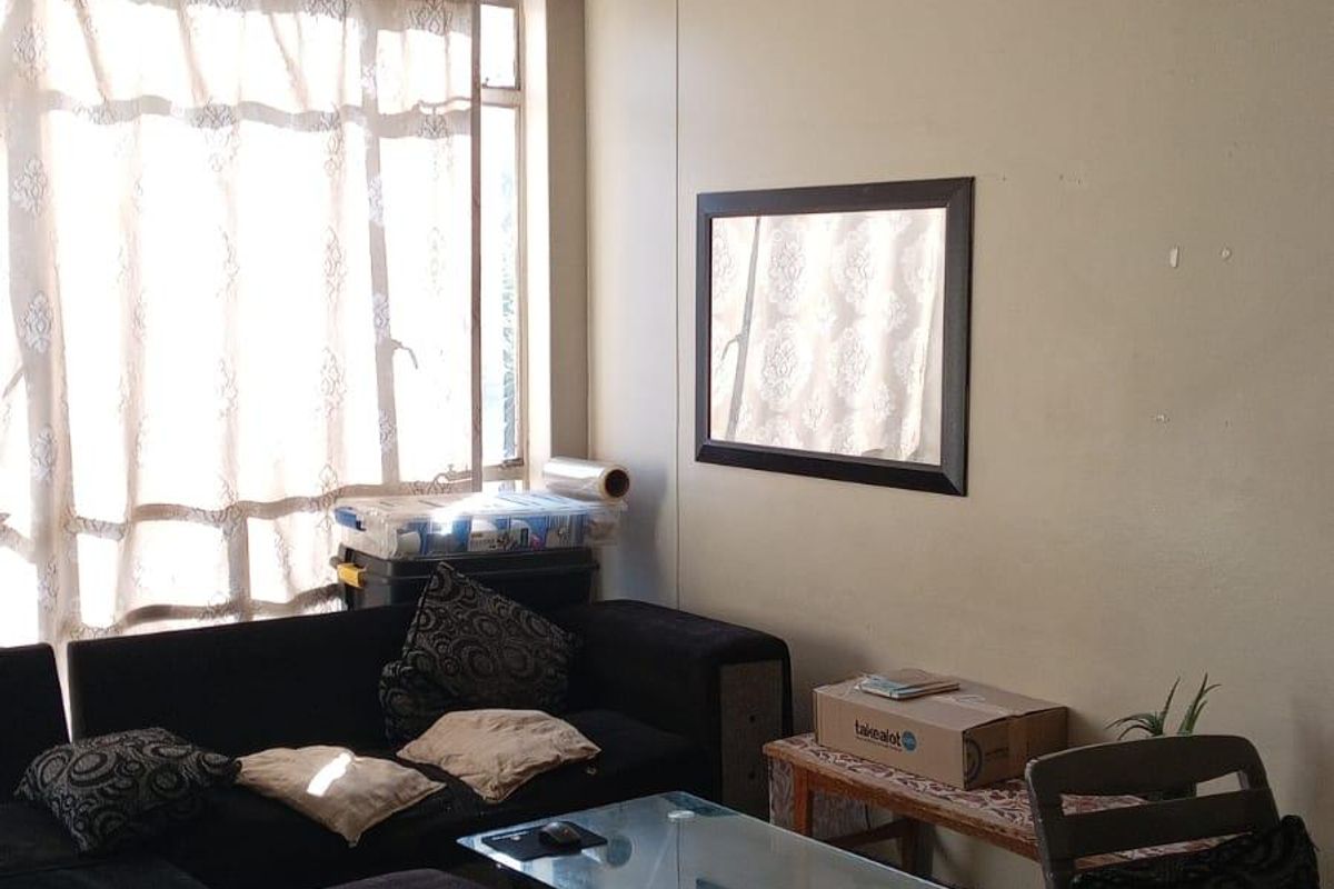 A living room area featuring tiled flooring and natural light from a large window, providing a functional space for relaxation.