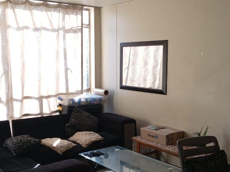 A living room area featuring tiled flooring and natural light from a large window, providing a functional space for relaxation.
