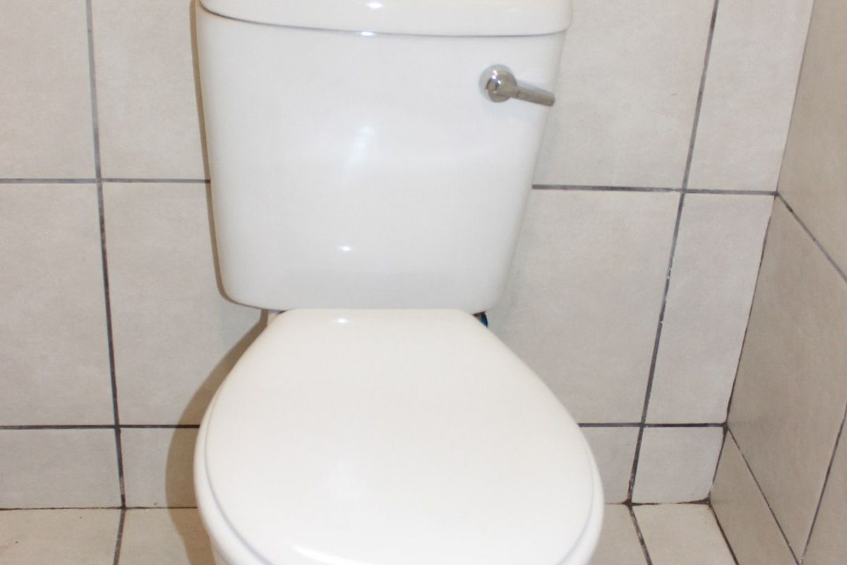 A functional bathroom space featuring a standard white toilet with neutral ceramic wall and floor tiling.
