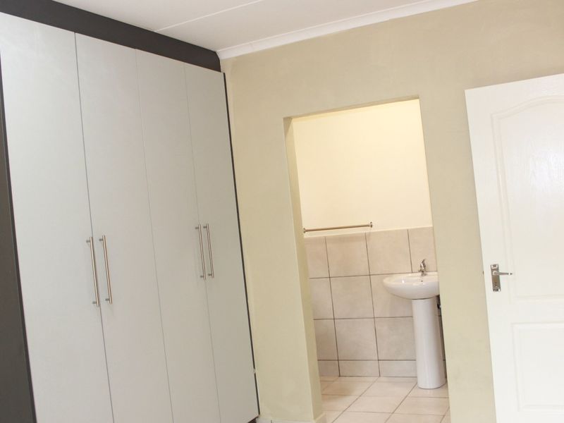 A bedroom featuring built-in cupboards and an en-suite bathroom area with a pedestal basin and tiled finishes.