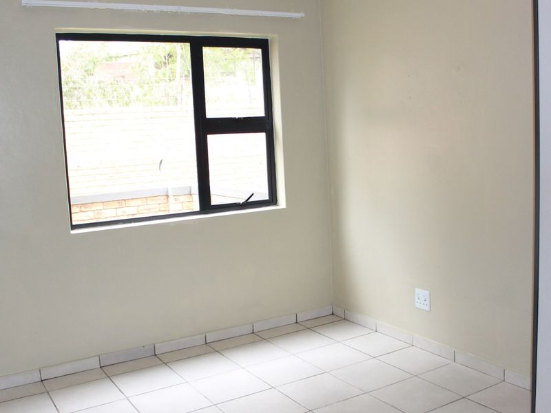 A clean, empty bedroom featuring neutral tiled flooring, a dark aluminium window frame, and a built-in cupboard.