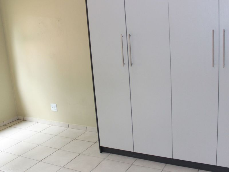 A bright, empty bedroom featuring neutral tiled flooring, a large built-in wardrobe with modern handles, and a window providing natural light.