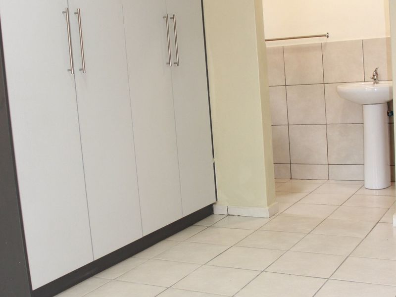 Bedroom featuring built-in cupboards and tiled flooring, with an adjoining en-suite bathroom area containing a pedestal basin.
