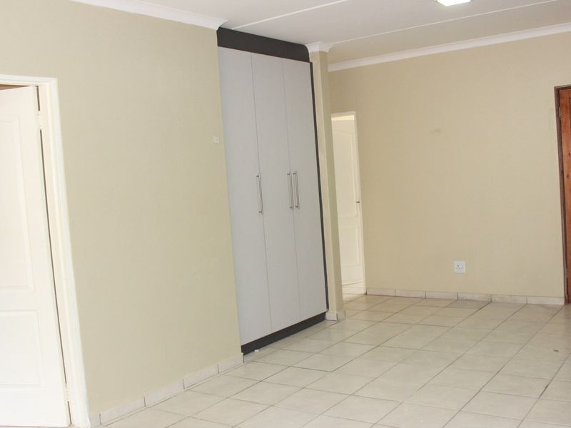 An open-plan living area featuring neutral walls, tiled flooring, and built-in storage cupboards, providing a clean and versatile space.
