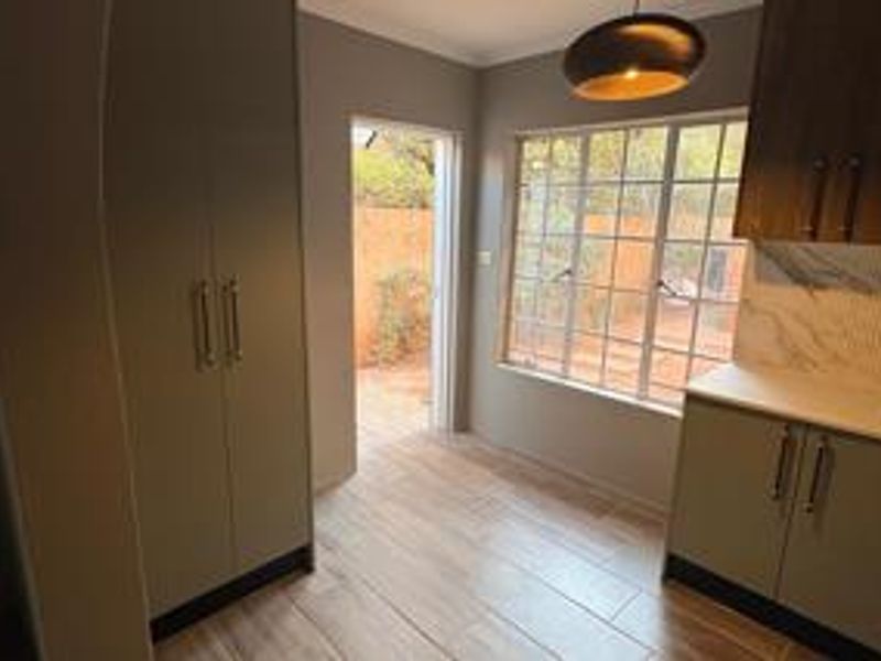 A clean, modern kitchen featuring neutral cabinetry, wood-look tiled flooring, and a window overlooking the rear garden area.