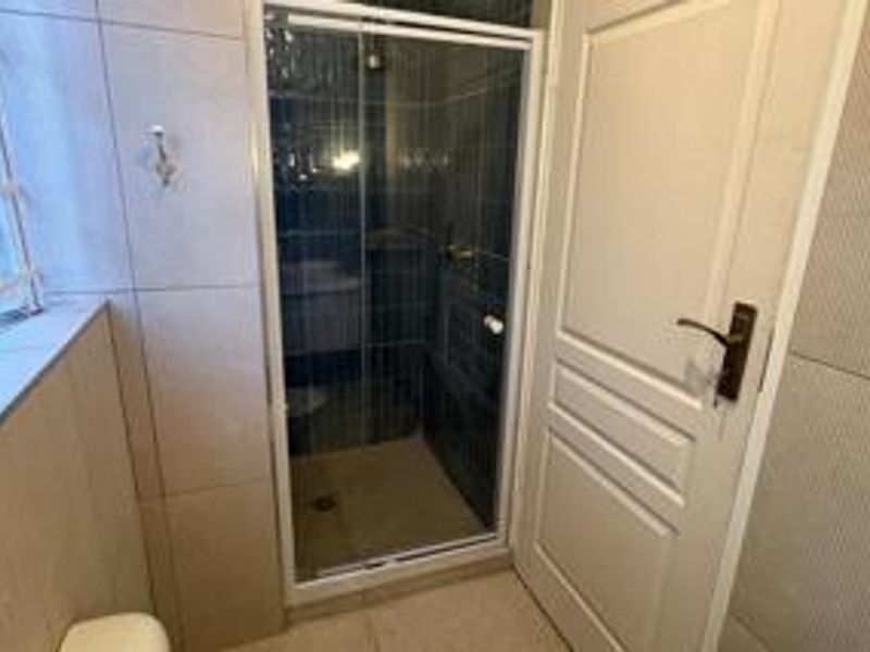 A functional bathroom featuring a glass-enclosed shower, neutral wall tiling, and a standard internal door.