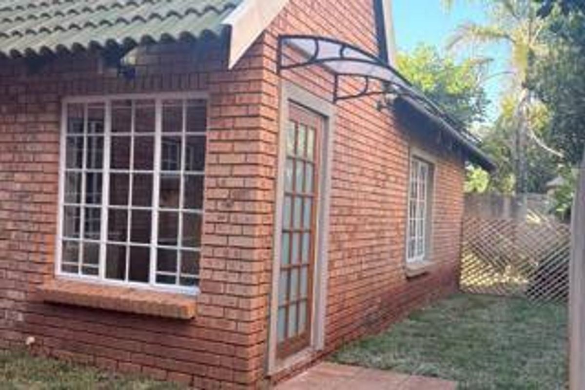 A view of the rear exterior of the apartment featuring face brick walls, a tiled roof, and a small garden area with lattice fencing.