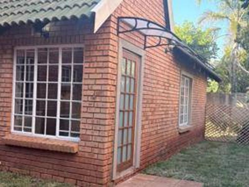 A view of the rear exterior of the apartment featuring face brick walls, a tiled roof, and a small garden area with lattice fencing.