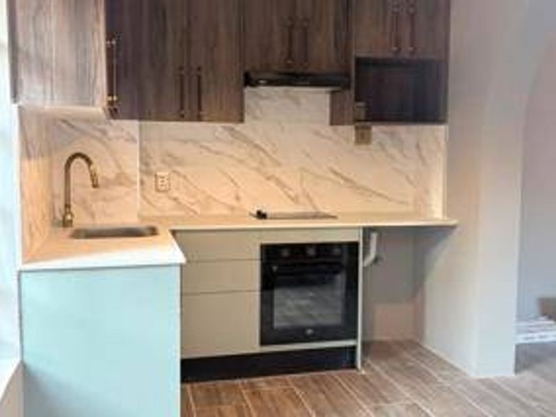 A modern kitchen featuring dark wood upper cabinetry, light base cabinets, marble-look backsplash, built-in oven, electric cooktop, and a sleek gooseneck faucet.