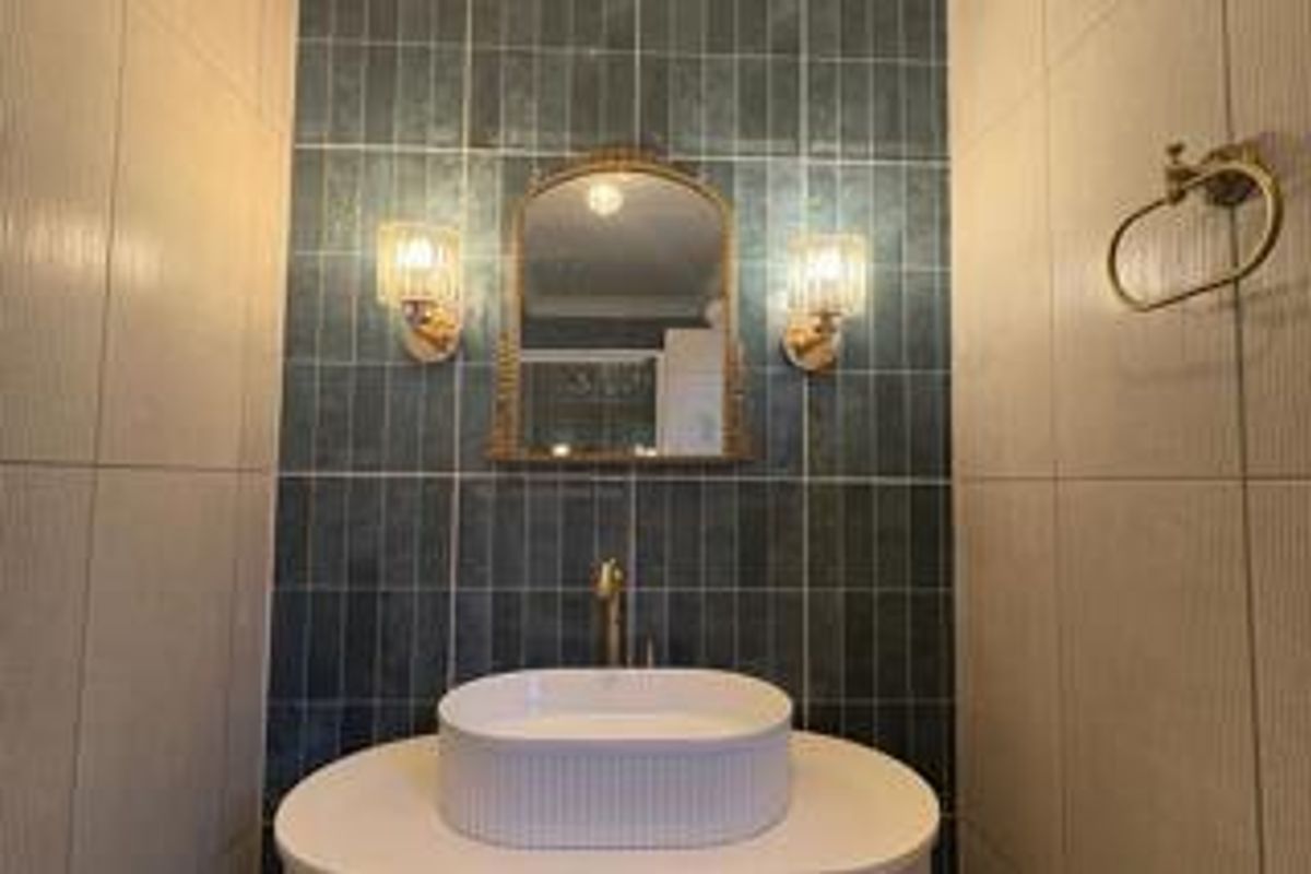 A modern bathroom featuring a stylish vessel sink, wall-mounted faucet, and a striking blue tiled feature wall with elegant sconce lighting.