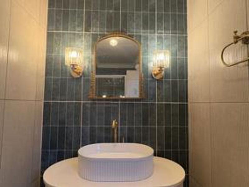 A modern bathroom featuring a stylish vessel sink, wall-mounted faucet, and a striking blue tiled feature wall with elegant sconce lighting.