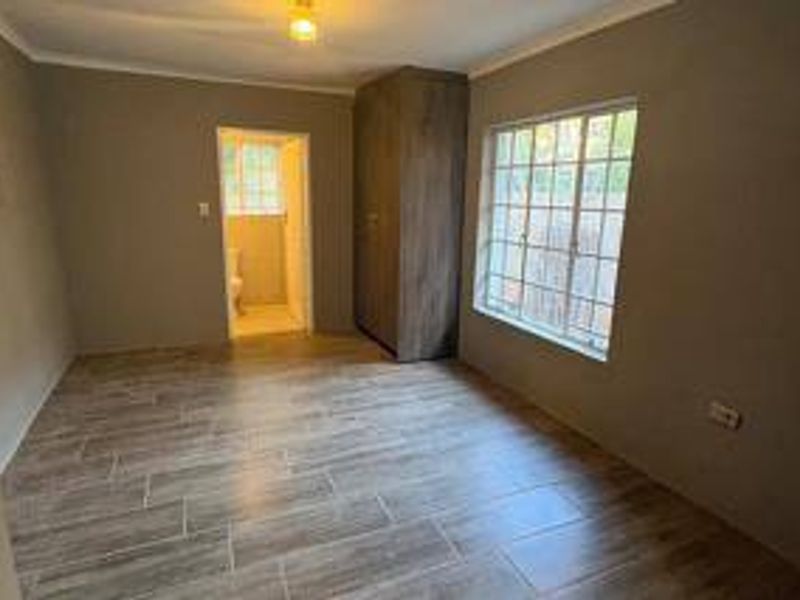 An empty bedroom featuring wood-look tiled flooring, a built-in wardrobe, and a window with security bars, with an adjacent bathroom visible.