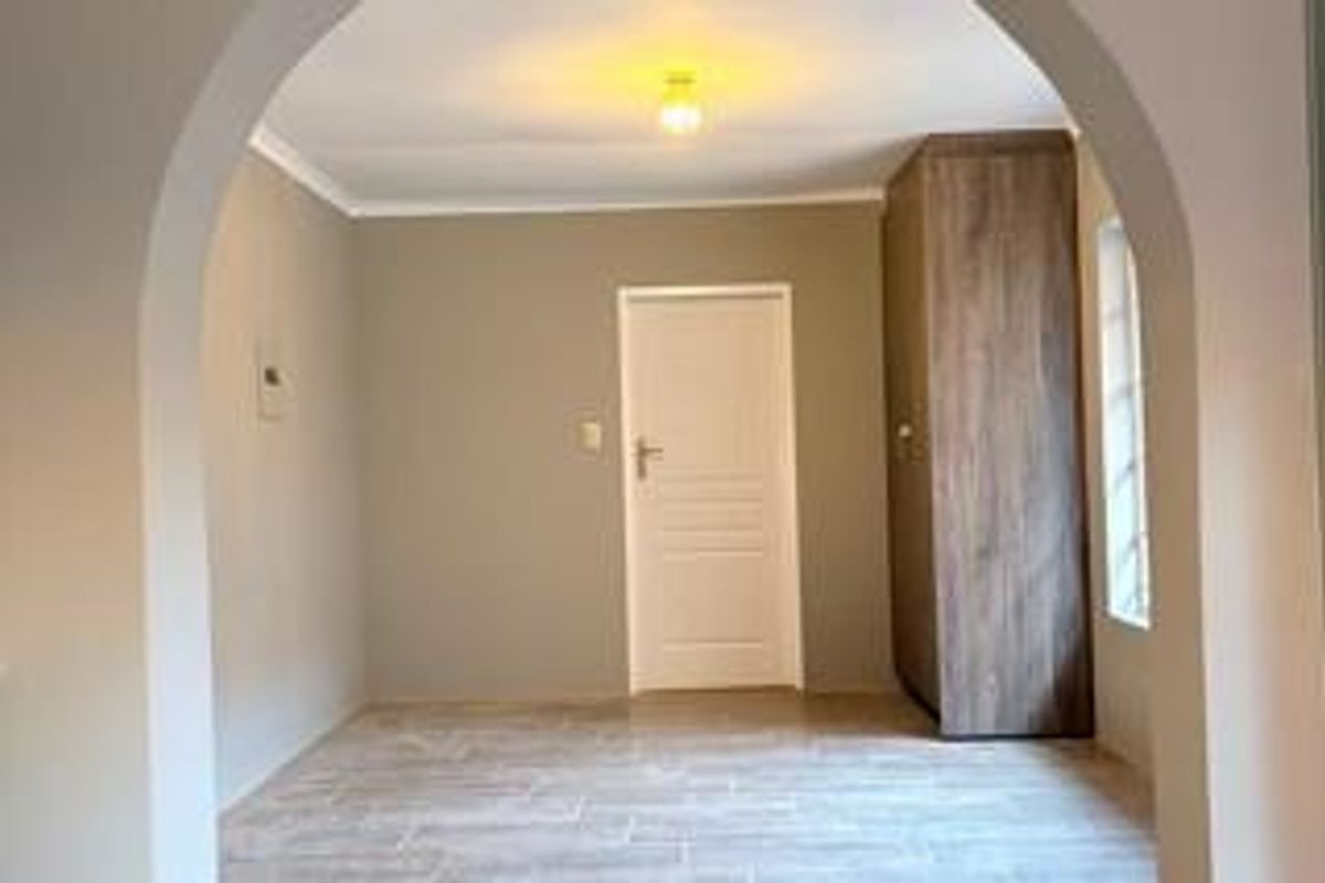 A bright, empty bedroom featuring neutral walls, tiled flooring, a built-in wooden wardrobe, and a distinctive arched entryway.