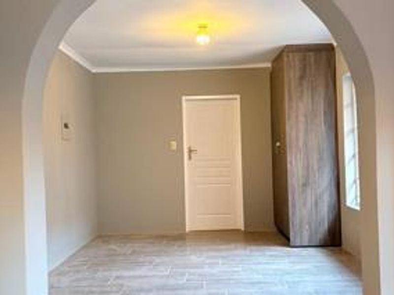 A bright, empty bedroom featuring neutral walls, tiled flooring, a built-in wooden wardrobe, and a distinctive arched entryway.