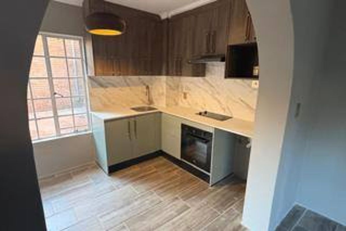 A modern, compact kitchen featuring wood-tone upper cabinets, light-colored lower cabinetry, marble-look backsplash, and integrated appliances including an oven and hob.