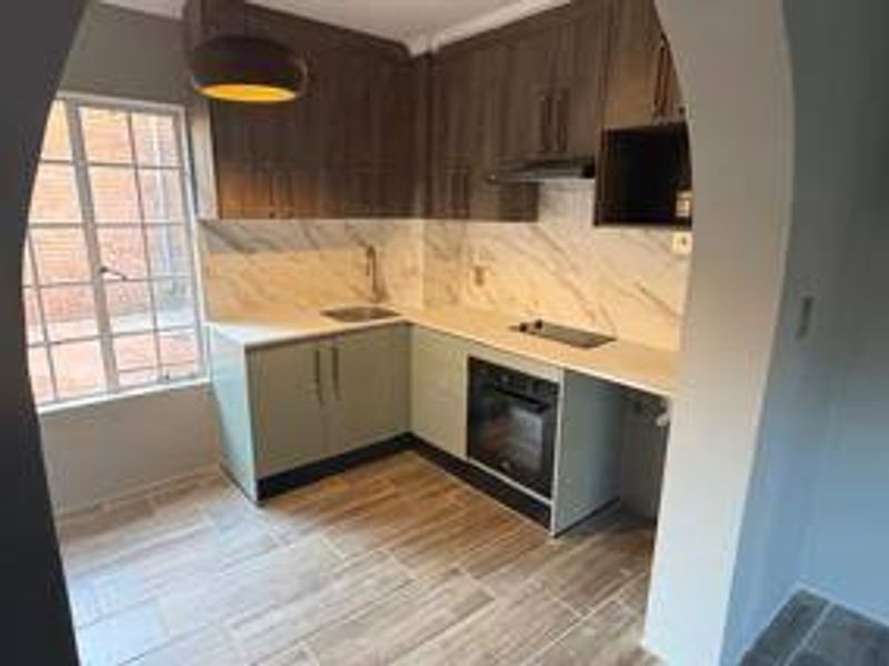 A modern, compact kitchen featuring wood-tone upper cabinets, light-colored lower cabinetry, marble-look backsplash, and integrated appliances including an oven and hob.
