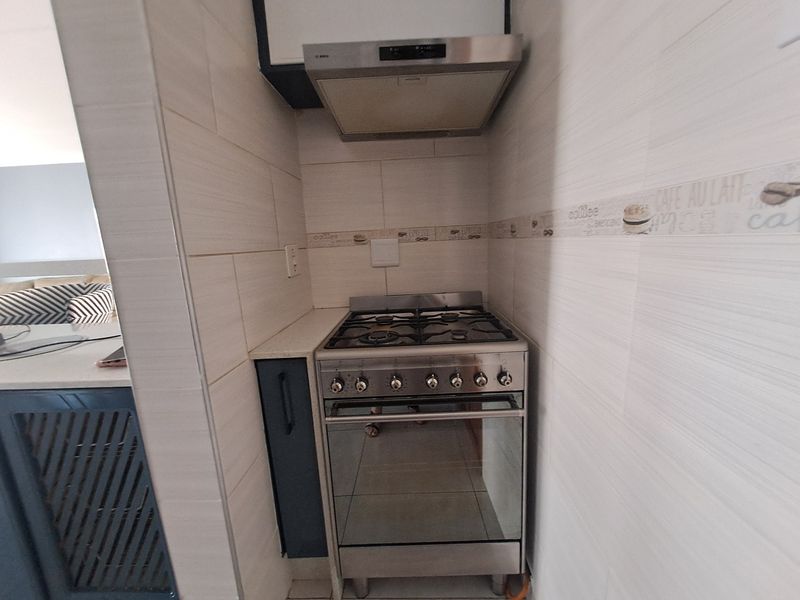 Compact kitchen area featuring a stainless steel gas stove, oven, and overhead extractor fan with modern tiled wall finishes.