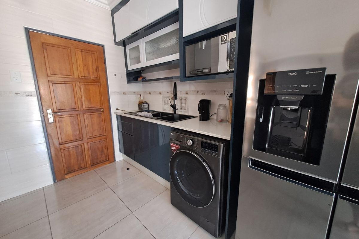 Modern kitchen area featuring sleek dark cabinetry, tiled flooring, integrated microwave, and a functional sink setup with a wooden door entrance.