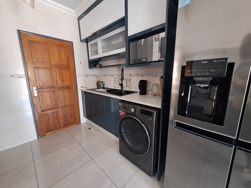 Modern kitchen area featuring sleek dark cabinetry, tiled flooring, integrated microwave, and a functional sink setup with a wooden door entrance.