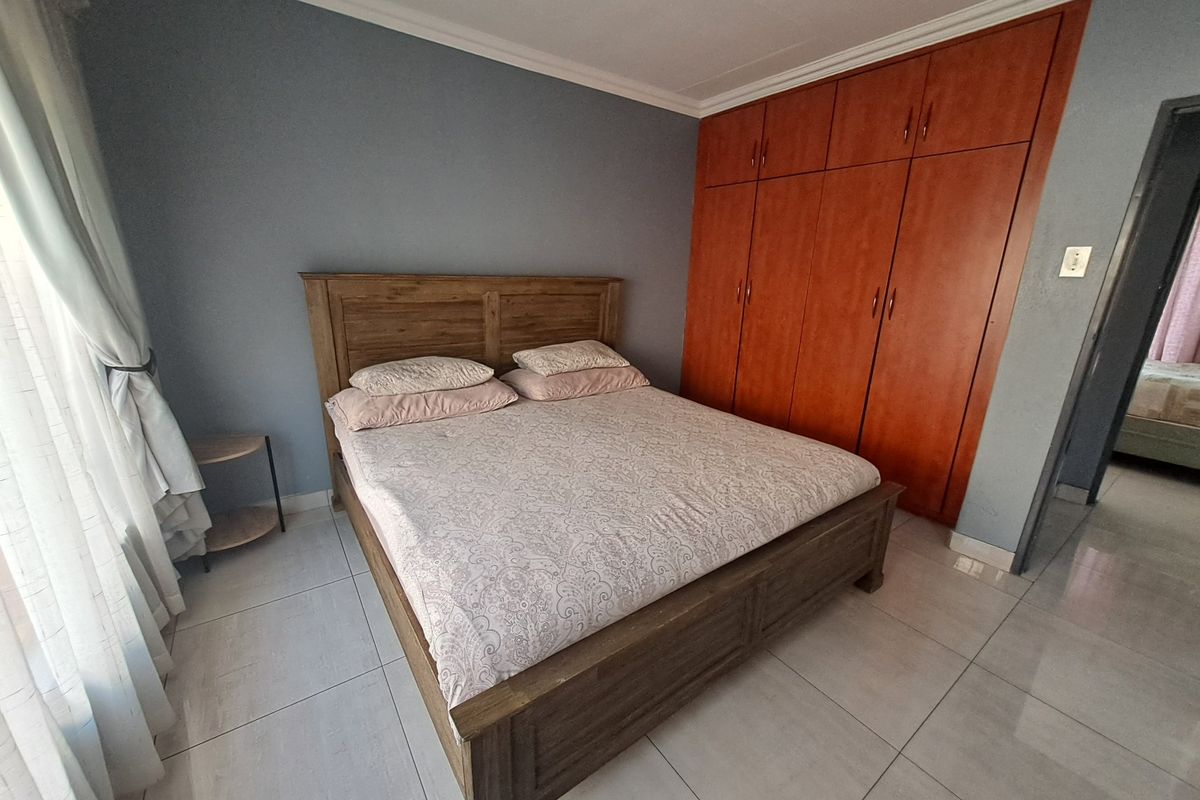A bedroom featuring built-in wooden cupboards, tiled flooring, and neutral wall finishes.