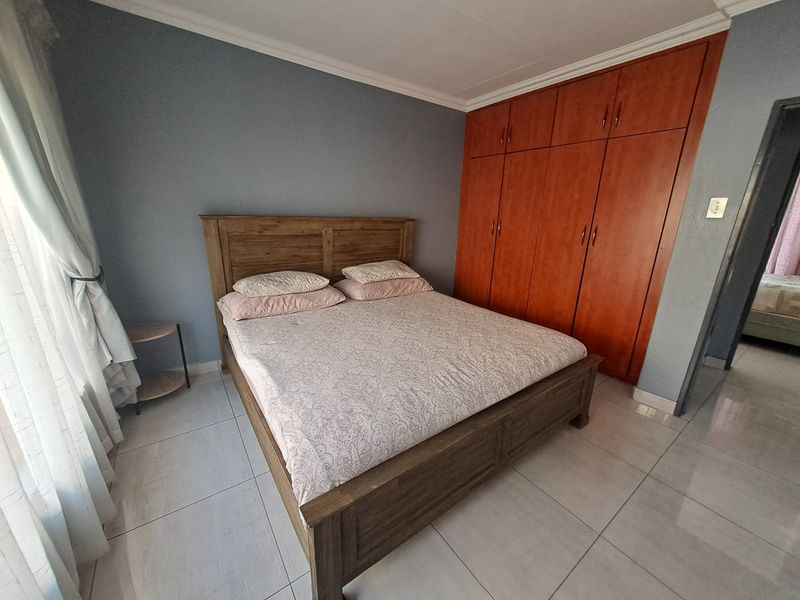 A bedroom featuring built-in wooden cupboards, tiled flooring, and neutral wall finishes.