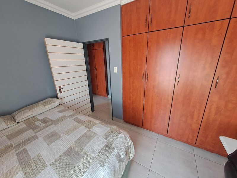 A bedroom featuring built-in wooden cupboards, tiled flooring, and decorative ceiling cornicing, with an adjacent doorway leading to a secondary storage area.