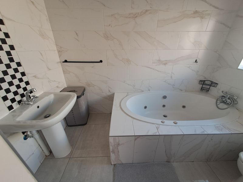 A modern bathroom featuring a pedestal basin, marble-look wall tiles, and a built-in jet bathtub with integrated fixtures.