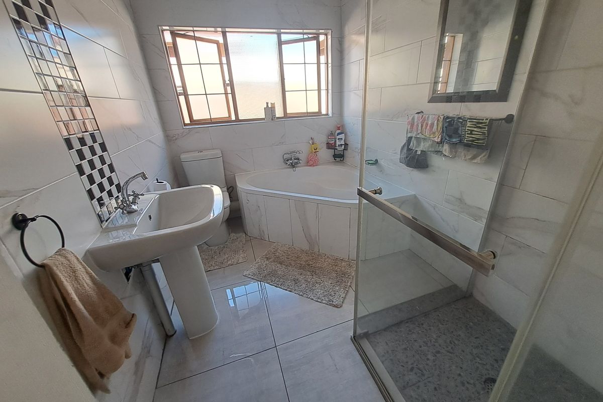 A well-appointed bathroom featuring a corner bathtub, a separate glass-enclosed shower, and a pedestal basin with modern wall tiling.