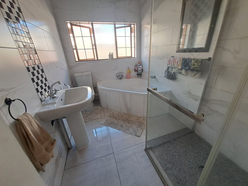 A well-appointed bathroom featuring a corner bathtub, a separate glass-enclosed shower, and a pedestal basin with modern wall tiling.