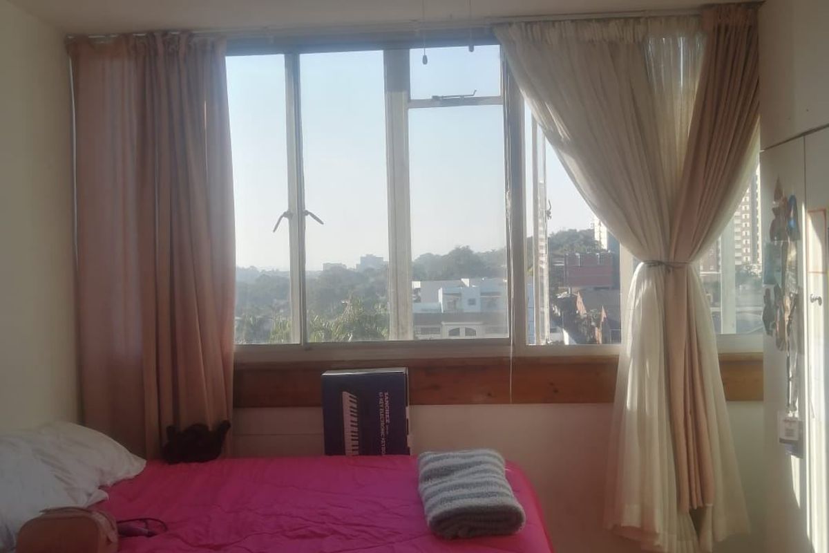 A bedroom featuring tiled flooring, a ceiling fan, and a large window providing natural light and an urban view.