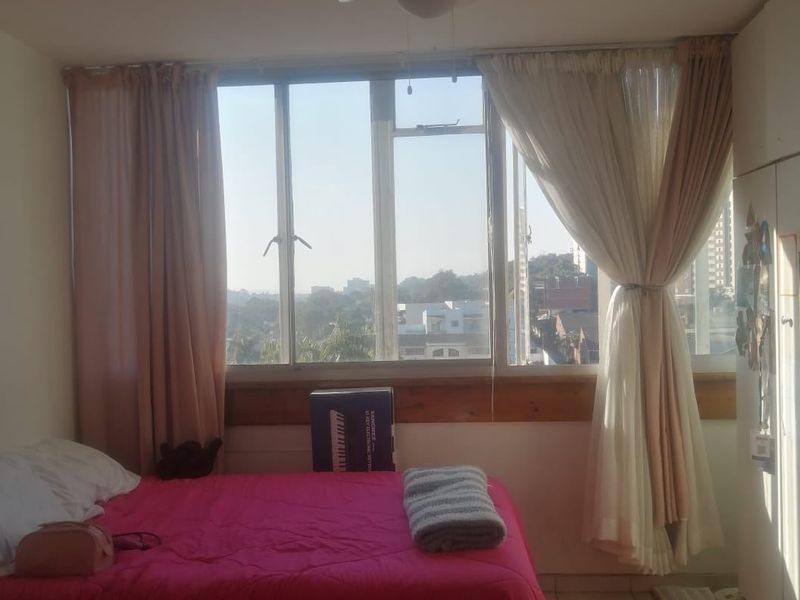 A bedroom featuring tiled flooring, a ceiling fan, and a large window providing natural light and an urban view.