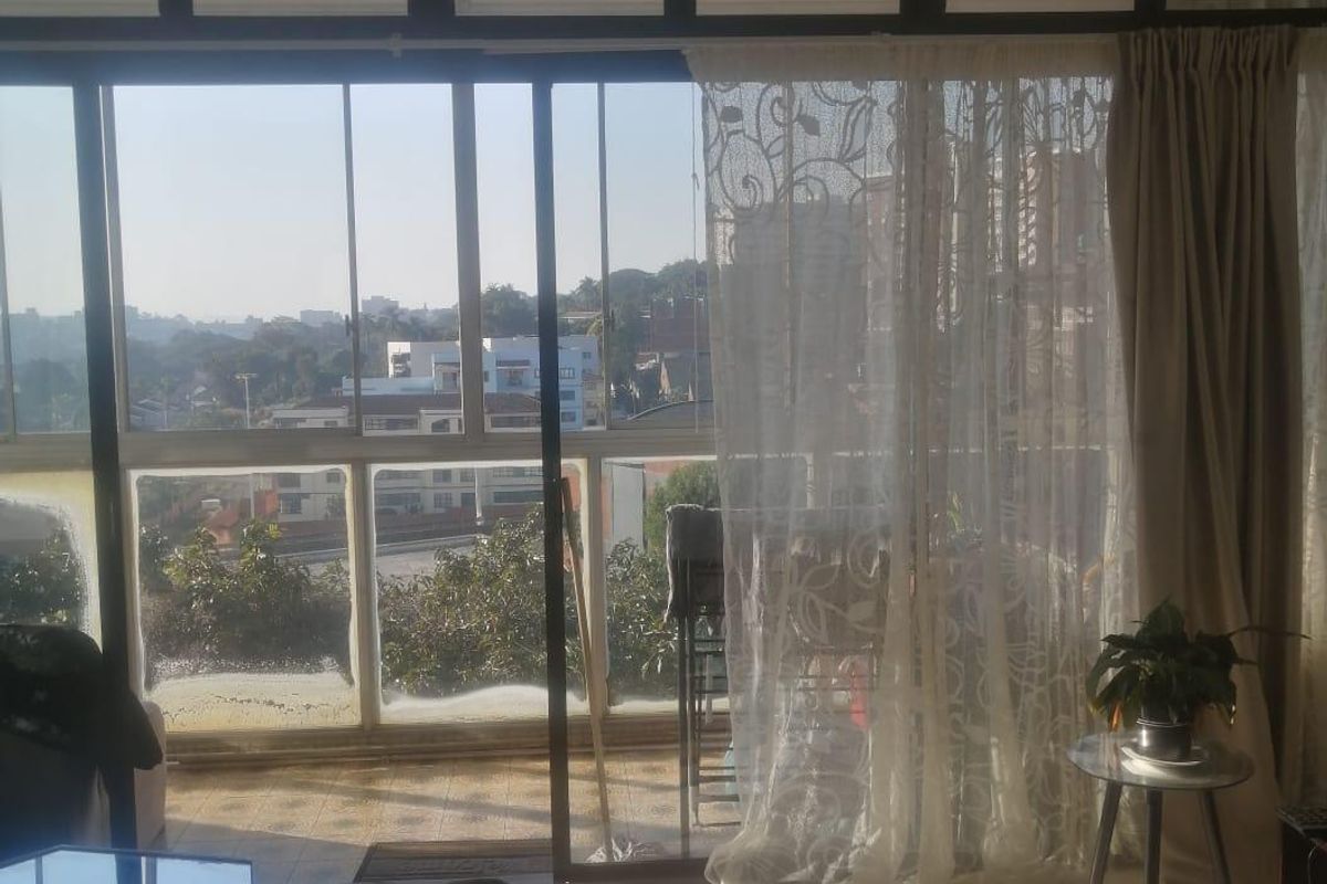 Living room featuring large sliding glass doors leading to a balcony, tiled flooring, and a ceiling fan, offering natural light and urban views.