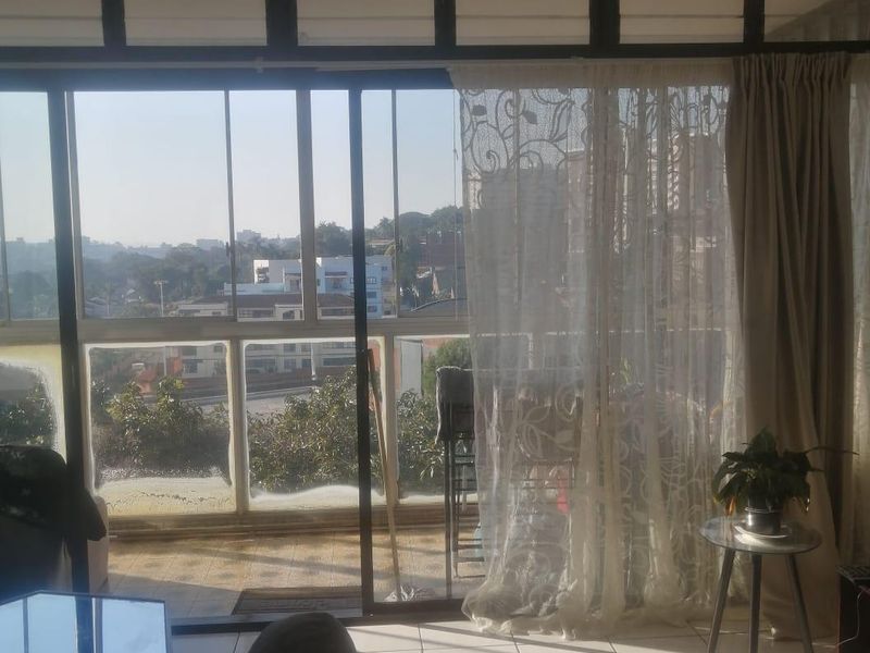 Living room featuring large sliding glass doors leading to a balcony, tiled flooring, and a ceiling fan, offering natural light and urban views.