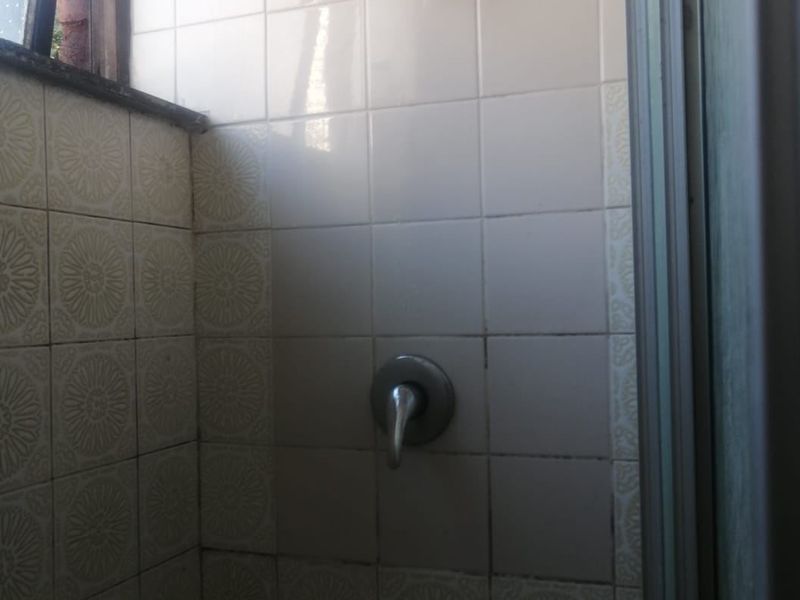 A compact shower enclosure featuring dated ceramic wall tiles and standard chrome shower fixtures.