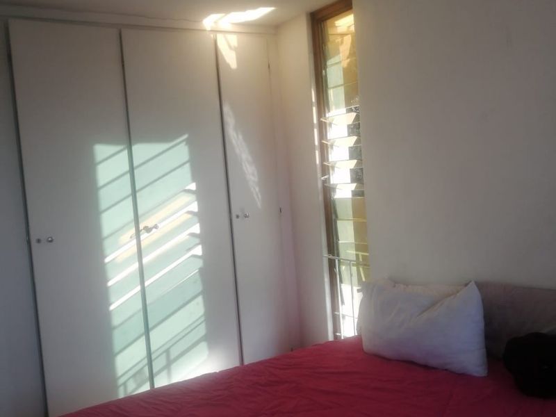 A bedroom featuring built-in cupboards and a louvered window, providing natural light and storage space.
