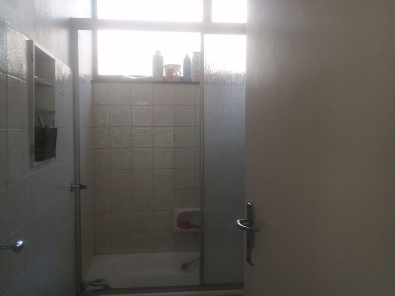 A functional bathroom featuring a bathtub with a glass shower screen, tiled walls, and a transom window for natural light.